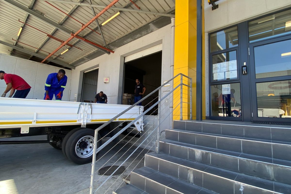Industrial facility exterior featuring a loading bay with roller shutter access, concrete hardstand, and a modern tiled entrance with glass door.