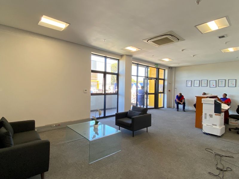 A bright, open-plan office reception area featuring carpeted floors, recessed lighting, cassette air conditioning, and large aluminium-framed windows providing natural light.