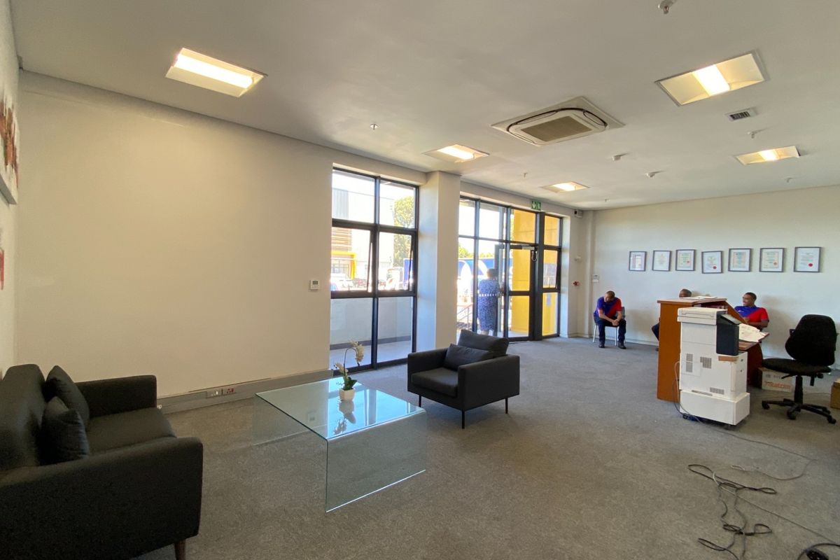 A bright, open-plan office reception area featuring carpeted floors, recessed lighting, cassette air conditioning, and large aluminium-framed windows providing natural light.