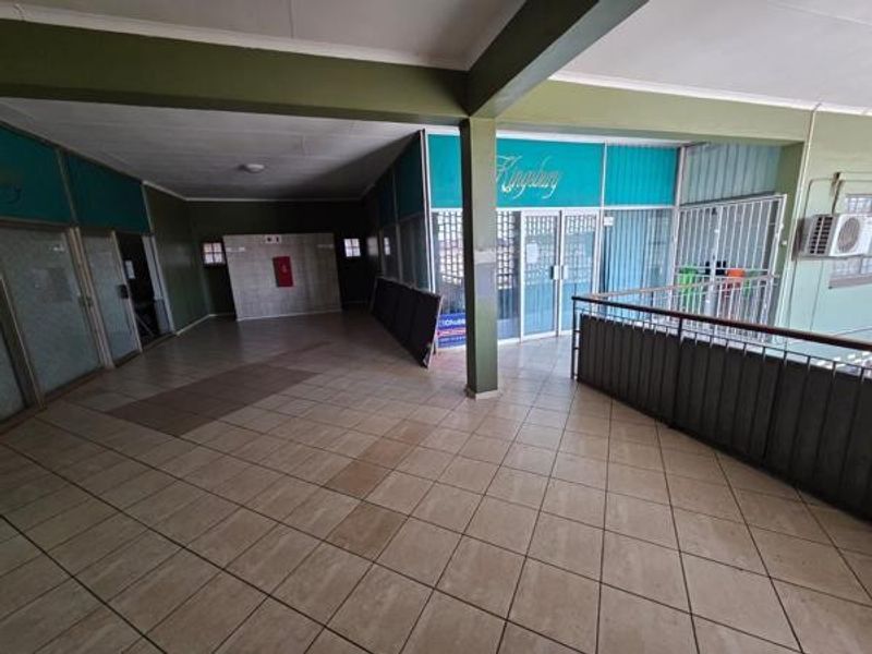 Spacious office building hallway featuring tiled flooring, glass partitions, and a metal security railing, providing access to multiple office units.