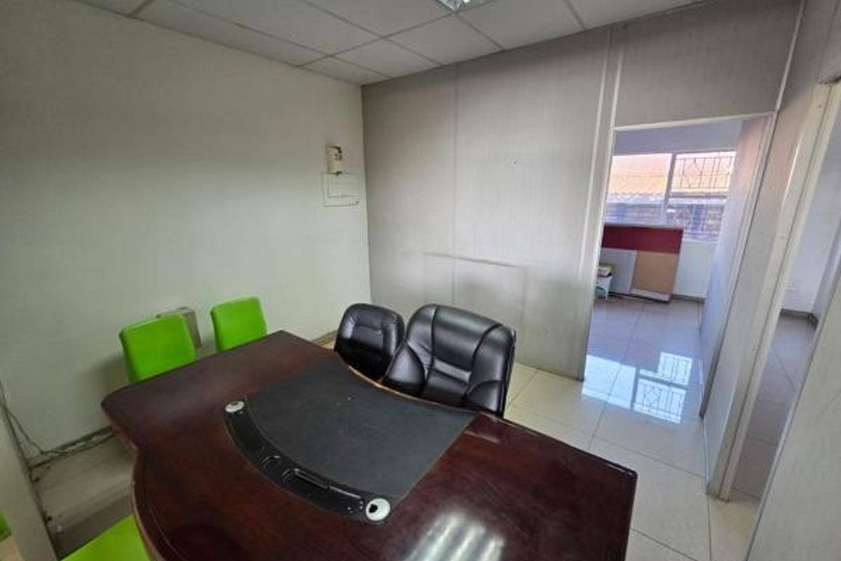 A functional office space featuring suspended ceilings, fluorescent lighting, and tiled flooring, with an adjacent room visible through the doorway.