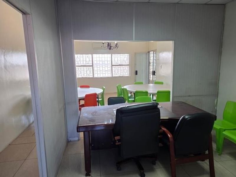 An office space featuring a partition wall, tiled flooring, and security bars on the windows, providing a functional layout for a workspace.