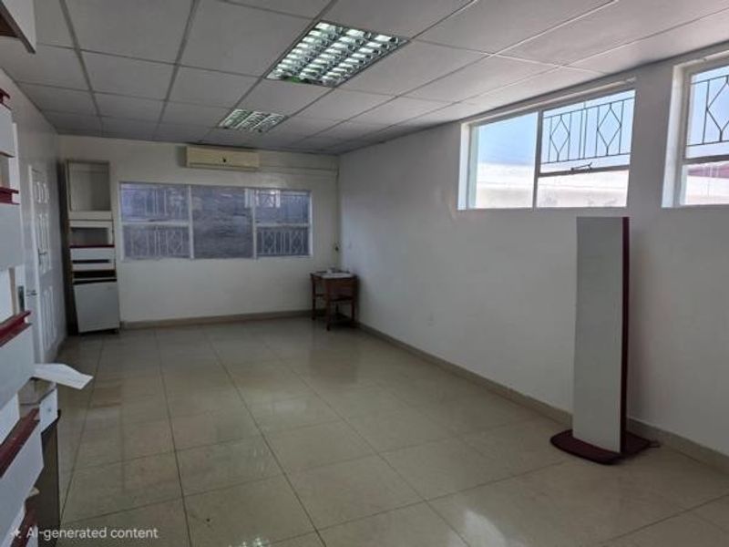 A spacious, vacant office area featuring tiled flooring, suspended ceilings with recessed lighting, and a wall-mounted air conditioning unit.