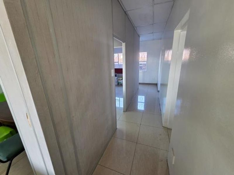 A functional office hallway featuring tiled flooring, partitioned walls, and a suspended ceiling, providing access to adjacent office spaces.