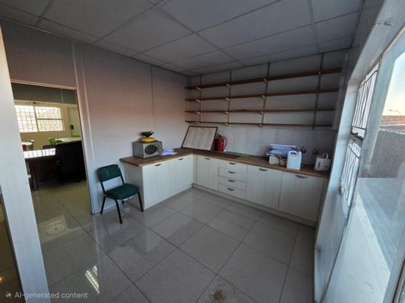 A functional office kitchenette featuring l-shaped cabinetry, open wall shelving, tiled flooring, and a drop ceiling, providing a practical break area for staff.