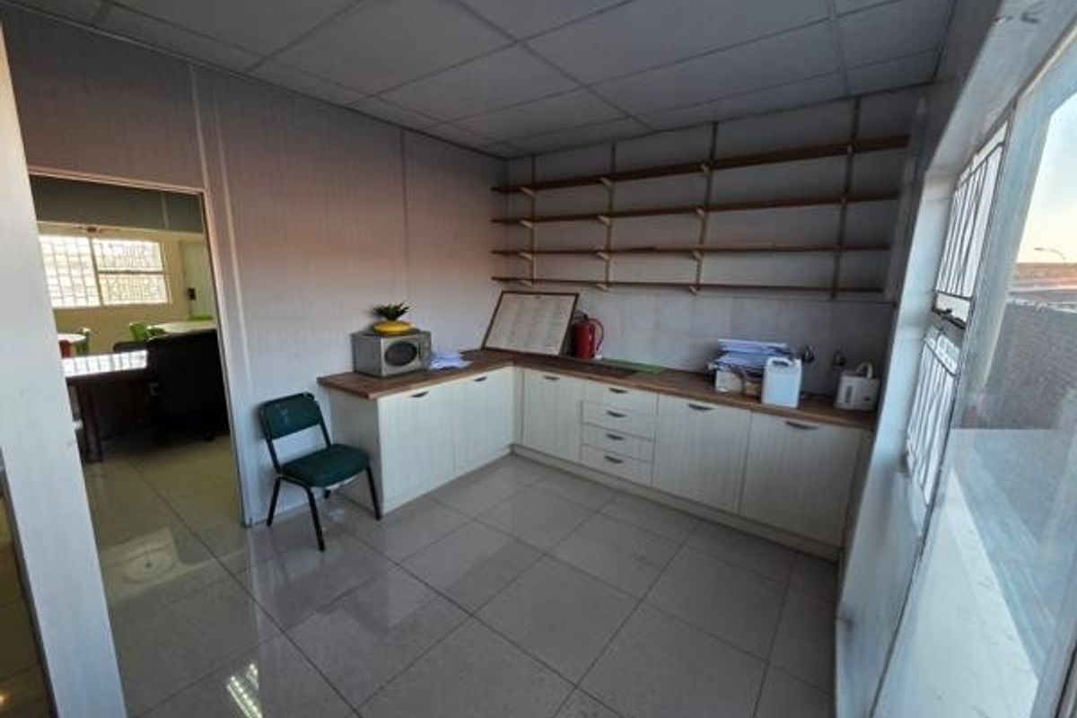 A functional office kitchenette featuring l-shaped cabinetry, open wall shelving, tiled flooring, and a drop ceiling, providing a practical break area for staff.