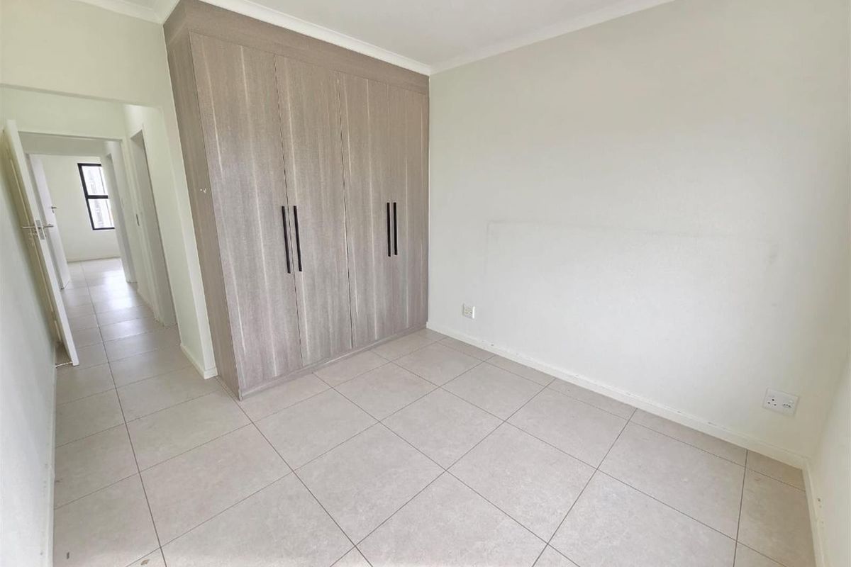 A bright, empty bedroom featuring neutral tiled flooring and modern built-in cupboards with sleek black handles.
