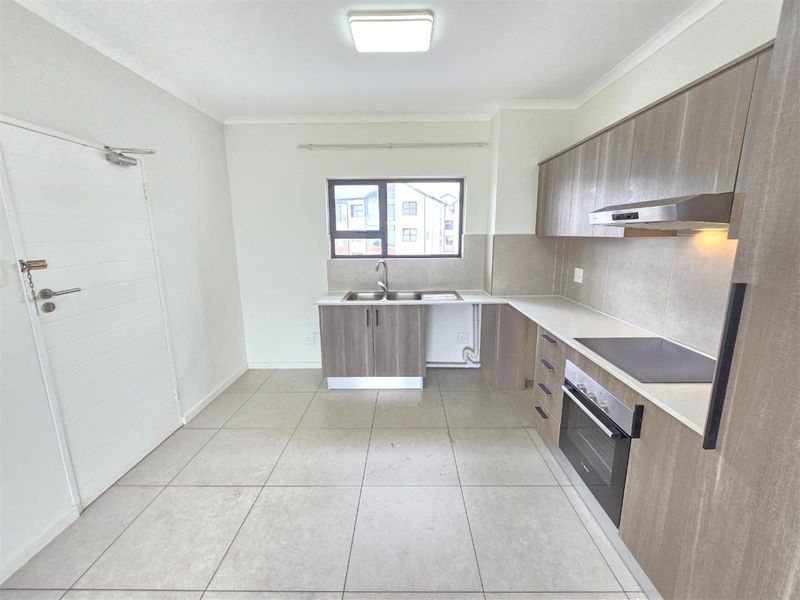 Modern kitchen featuring neutral cabinetry, built-in oven, electric hob, extractor fan, and tiled flooring in a clean, open-plan layout.