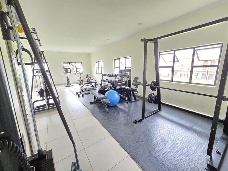 A spacious, well-lit private gym featuring a combination of tiled and rubber flooring, equipped with multiple windows for natural ventilation.
