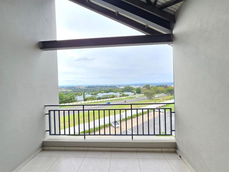 A covered balcony featuring tiled flooring and a metal balustrade, offering an elevated view of the surrounding landscape and road.