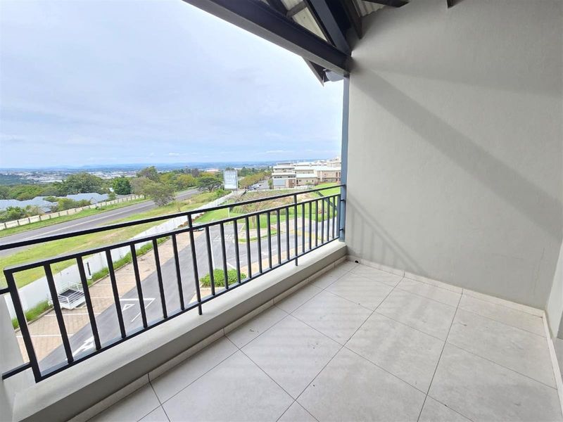 A spacious covered balcony featuring tiled flooring, a secure metal balustrade, and elevated views of the surrounding neighborhood and landscape.