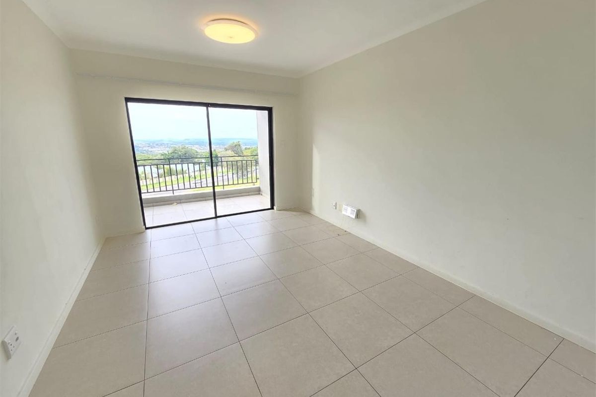 A bright, empty living area featuring neutral tiled flooring and a large sliding glass door that opens onto a balcony with scenic views.