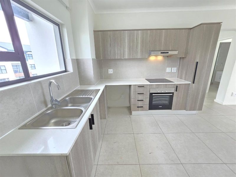 Modern kitchen featuring light wood-grain cabinetry, stone countertops, built-in oven, electric hob, and a double bowl stainless steel sink.