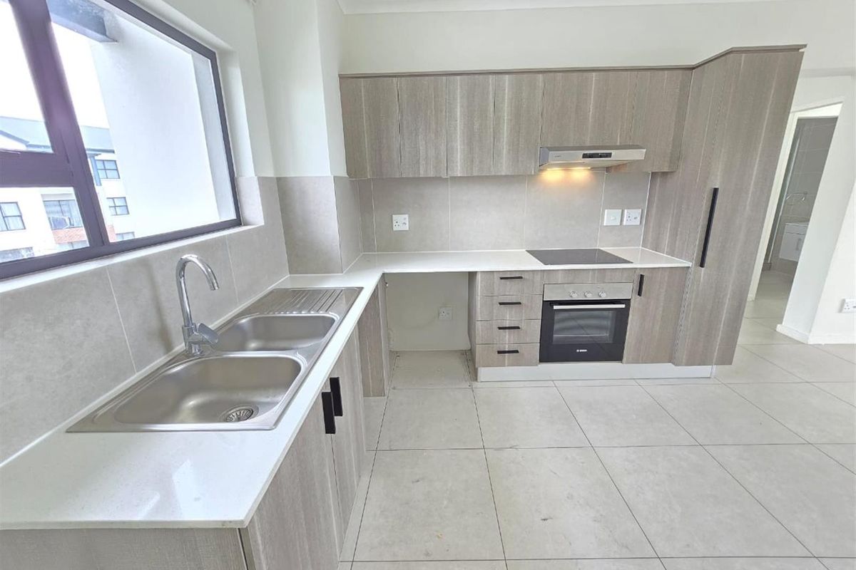 Modern kitchen featuring light wood-grain cabinetry, stone countertops, built-in oven, electric hob, and a double bowl stainless steel sink.