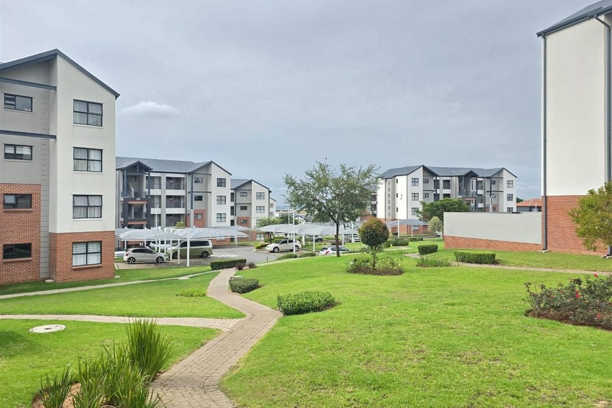 A view of the apartment complex grounds featuring well-maintained lawns, paved walkways, and covered parking bays between the residential buildings.
