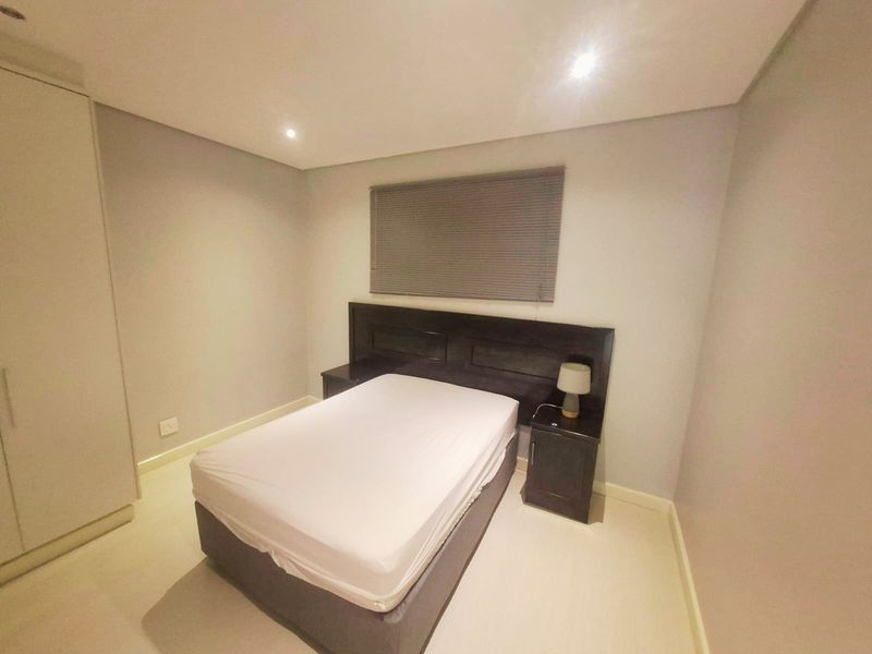A clean and modern bedroom featuring neutral walls, recessed downlighting, a built-in wardrobe, and a fitted window blind.