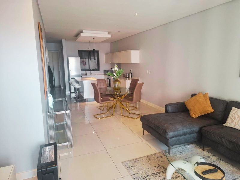 Modern open-plan living area featuring a sleek kitchen with island, tiled flooring, and recessed lighting, creating a bright and functional space.