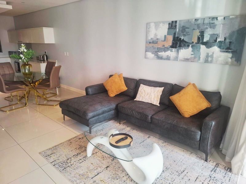 A modern open-plan living and dining area featuring sleek tiled flooring, recessed ceiling lights, and a contemporary kitchen with built-in cabinetry.