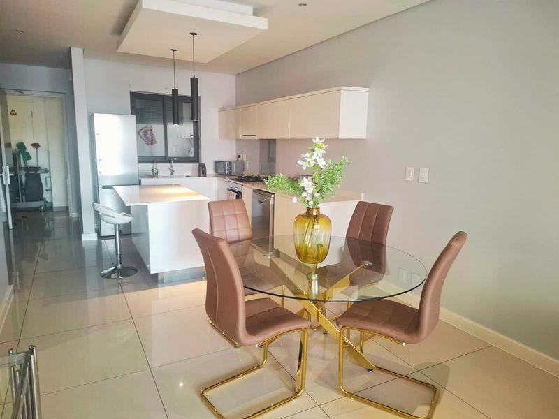 Modern open-plan kitchen and dining area featuring sleek cabinetry, a central island, and high-gloss tiled flooring, creating a bright and functional living space.