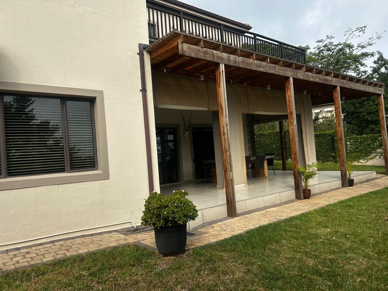 A spacious covered patio featuring a timber pergola, tiled flooring, and direct access to the garden through large sliding glass doors.