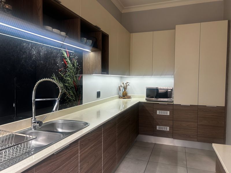 Modern kitchen featuring two-tone cabinetry, stone countertops, a double bowl sink with gooseneck faucet, and integrated under-cabinet lighting.