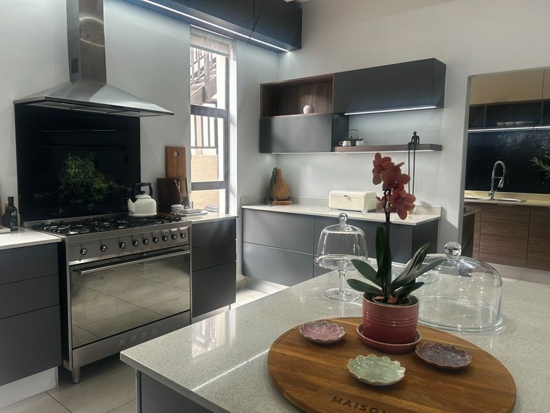 Modern kitchen featuring dark grey cabinetry, stone countertops, a large kitchen island, and a professional-style gas stove with an integrated extractor fan.
