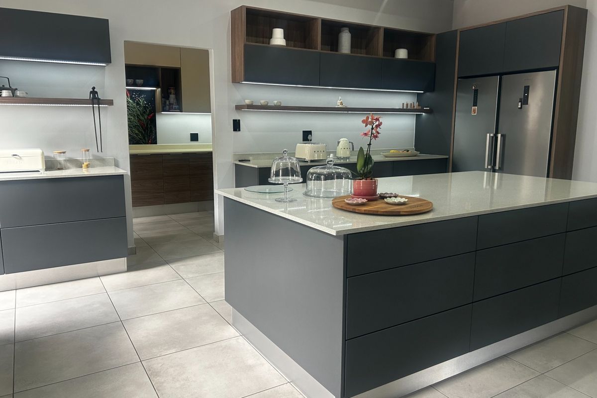 Modern kitchen featuring a large central island with quartz countertops, sleek dark cabinetry, integrated under-cabinet lighting, and high-quality tiled flooring.
