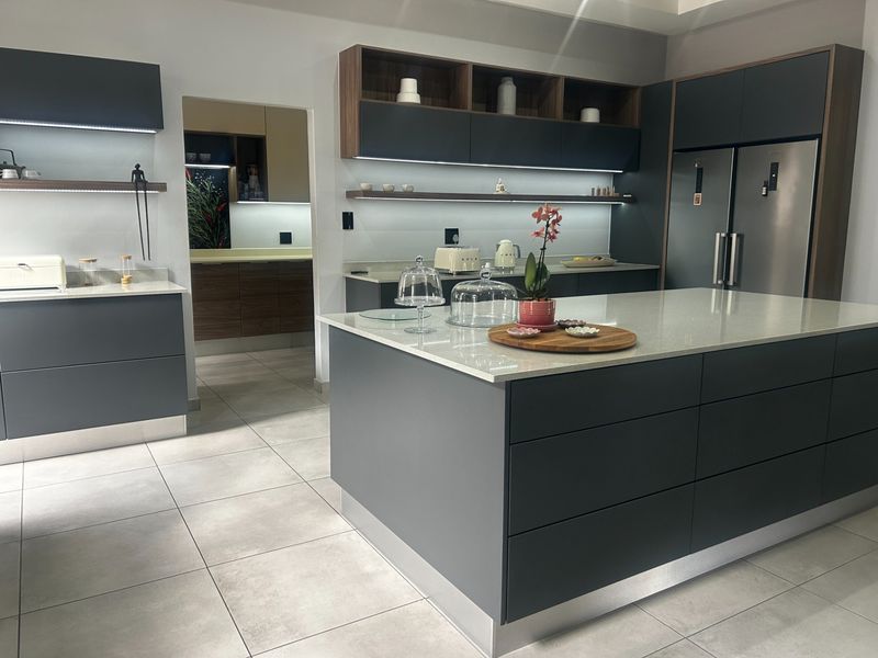 Modern kitchen featuring a large central island with quartz countertops, sleek dark cabinetry, integrated under-cabinet lighting, and high-quality tiled flooring.