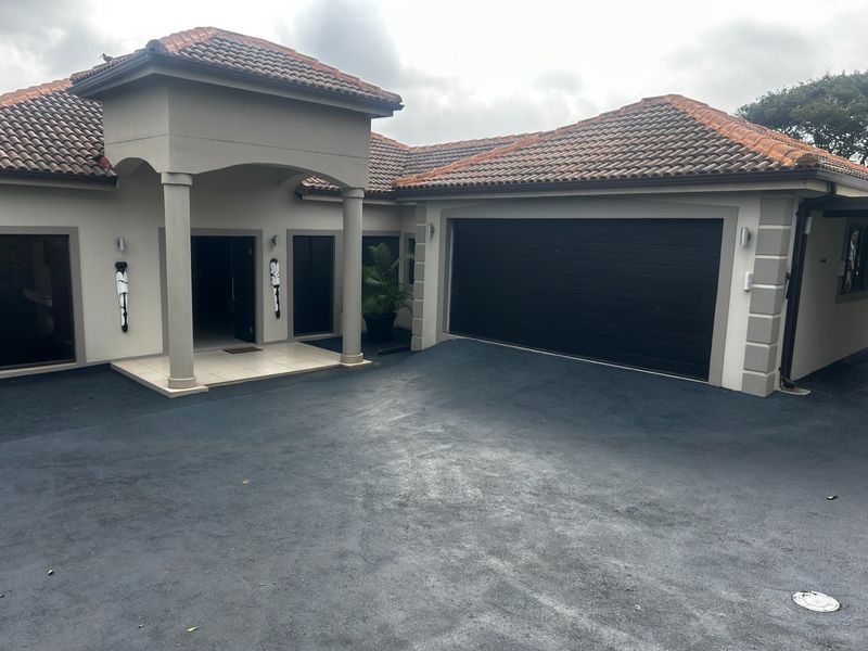 Front elevation of a residential house featuring a covered entrance, tiled roof, and a double garage with a paved driveway.