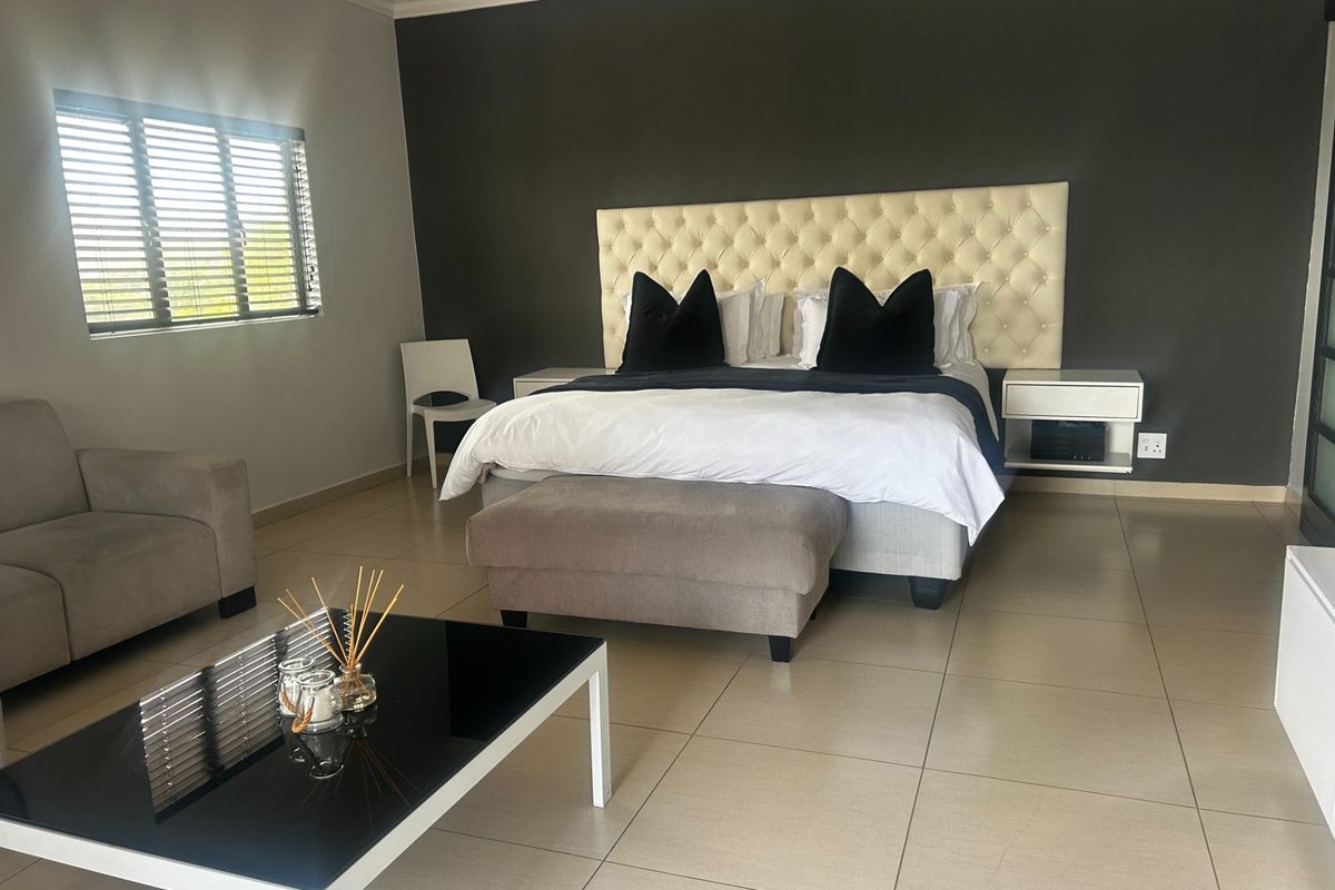 Spacious bedroom featuring tiled flooring, a large tufted headboard with integrated floating bedside tables, and venetian blinds.