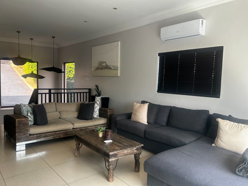 A comfortable living room featuring tiled flooring, a wall-mounted air conditioning unit, and a metal balustrade overlooking the entrance area.