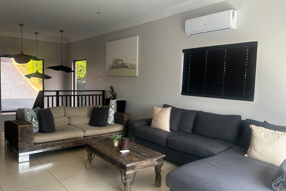 A comfortable living room featuring tiled flooring, a wall-mounted air conditioning unit, and a metal balustrade overlooking the entrance area.