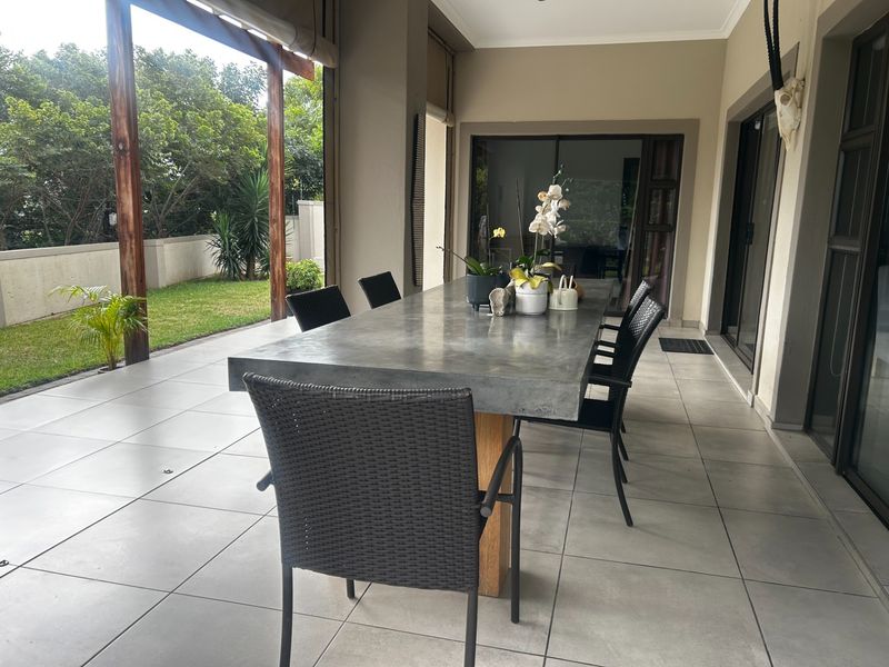 A spacious covered patio featuring large format floor tiles, timber support beams, and direct access to the garden through sliding glass doors.