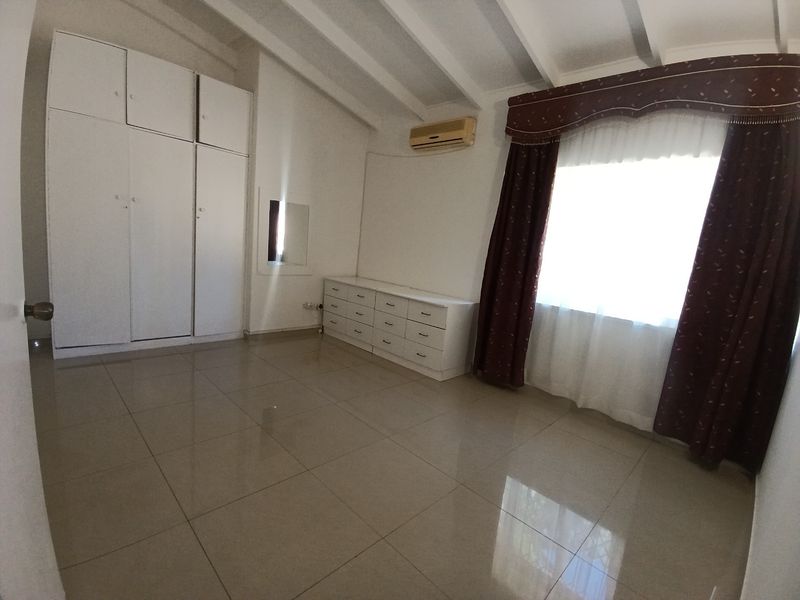 Spacious bedroom featuring tiled flooring, exposed ceiling beams, built-in cupboards, and a built-in dresser, offering a clean and functional layout.
