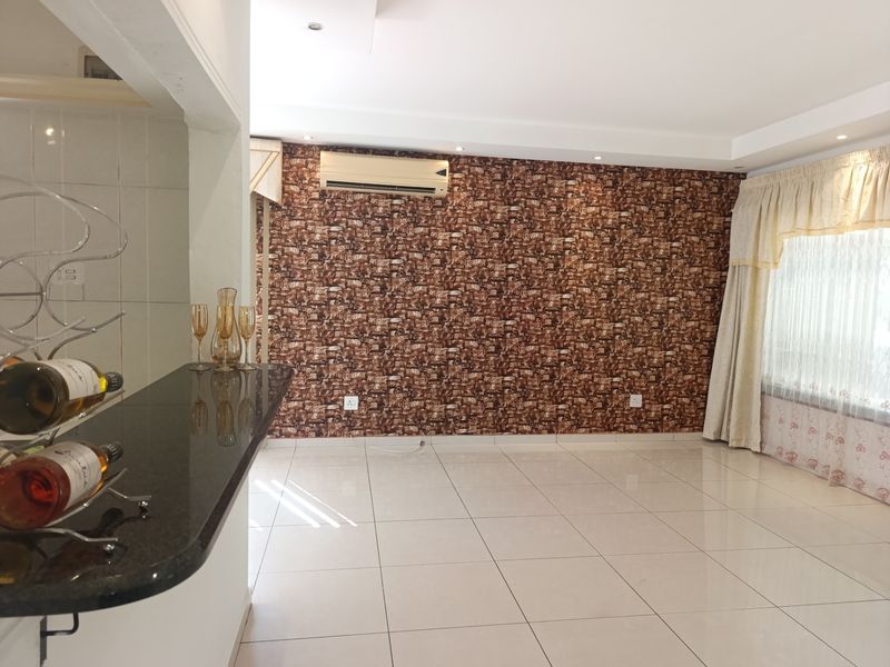 Spacious living area featuring tiled flooring, a granite breakfast bar, and a wall-mounted air conditioning unit, offering a clean and versatile layout.