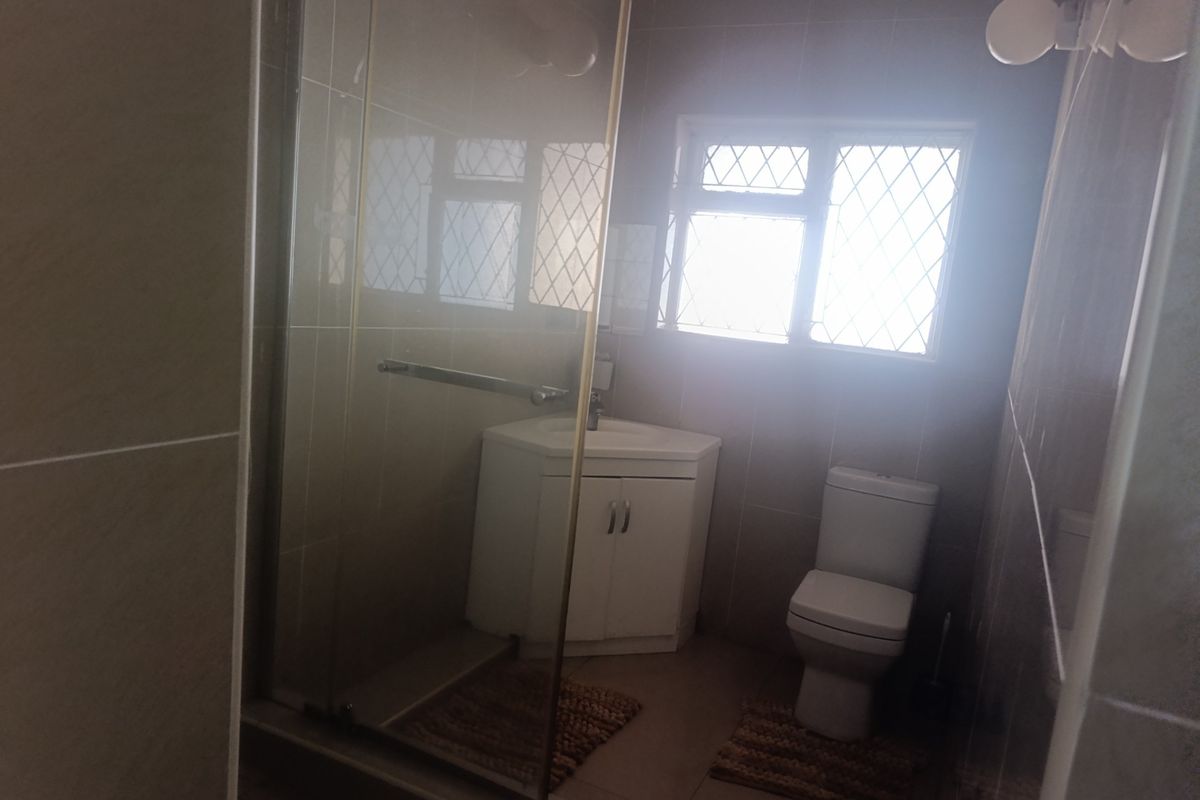 A functional bathroom featuring a glass shower enclosure, corner vanity unit, and toilet, finished with neutral wall and floor tiling.