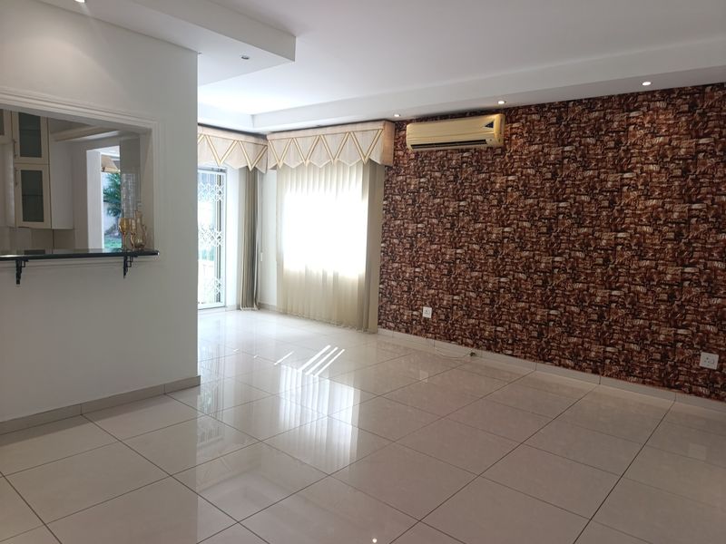 Spacious living area featuring polished porcelain tiles, a textured feature wall, split-system air conditioning, and a convenient pass-through window to the kitchen.