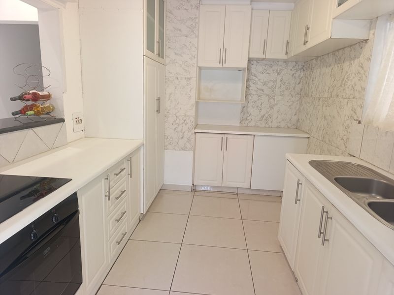 A functional kitchen featuring white built-in cabinetry, marble-effect wall tiling, a stainless steel double sink, and integrated oven with hob.