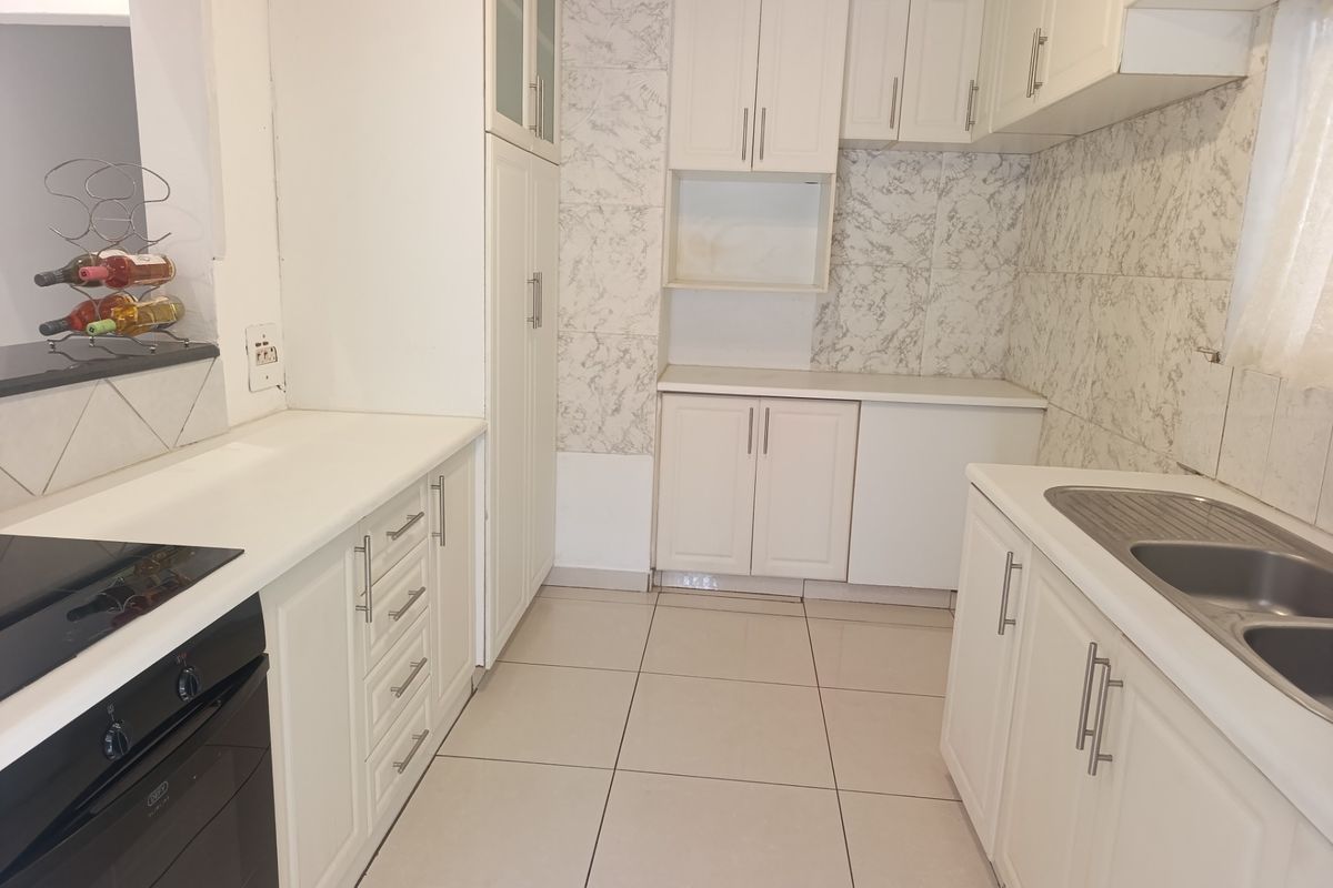 A functional kitchen featuring white built-in cabinetry, marble-effect wall tiling, a stainless steel double sink, and integrated oven with hob.