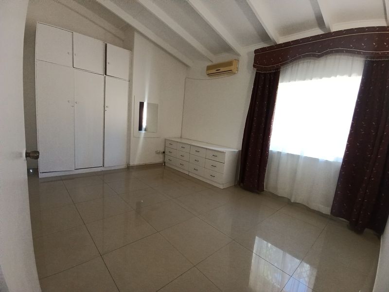 A spacious bedroom featuring tiled flooring, built-in cupboards, and an exposed beam ceiling, providing a clean and neutral foundation for personalization.