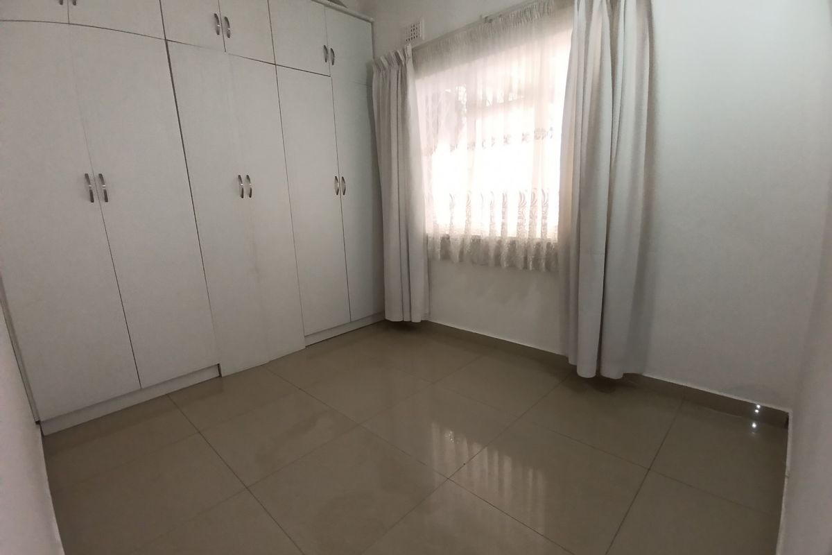 A clean, empty bedroom featuring neutral tiled flooring and extensive white built-in cupboards providing ample storage space.