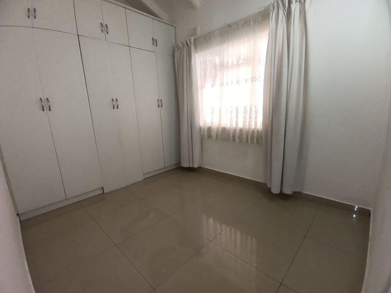 A clean, empty bedroom featuring neutral tiled flooring and extensive white built-in cupboards providing ample storage space.