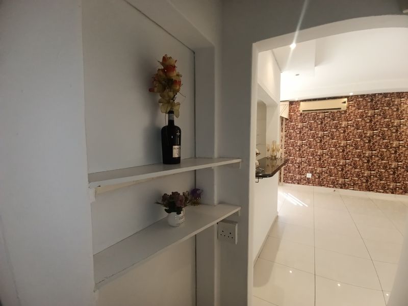 A hallway area featuring built-in shelving, leading into a living space with tiled floors, a feature wall, and a wall-mounted air conditioning unit.
