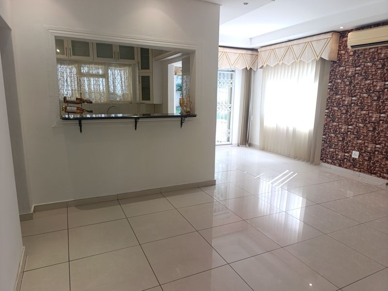 Spacious open-plan living area featuring polished tile floors, a convenient kitchen pass-through window with a breakfast bar, and modern recessed lighting.