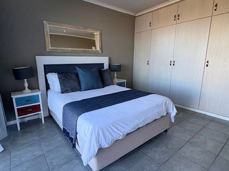 A well-maintained bedroom featuring neutral wall tones, tiled flooring, and extensive built-in cupboard storage.