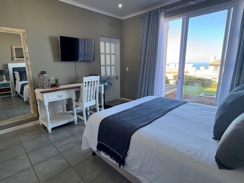 A well-lit bedroom featuring tiled flooring, recessed lighting, and a large sliding glass door providing access to an outdoor area with a sea view.