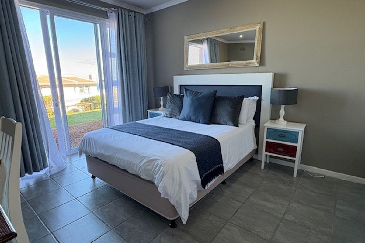 A well-lit bedroom featuring tiled flooring, neutral wall tones, and a large sliding glass door providing direct access to the outdoor area.