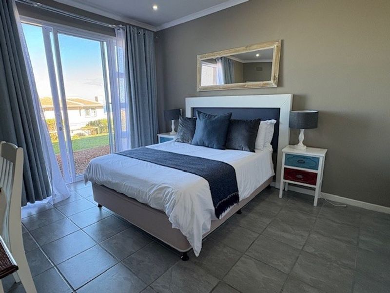A well-lit bedroom featuring tiled flooring, neutral wall tones, and a large sliding glass door providing direct access to the outdoor area.