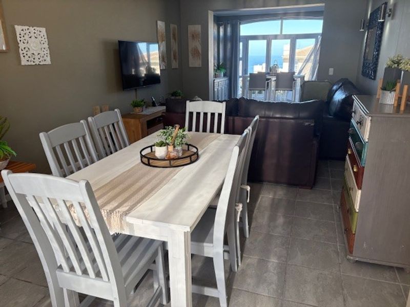Open plan dining and living area featuring tiled flooring and large sliding doors leading to an outdoor space with ocean views.