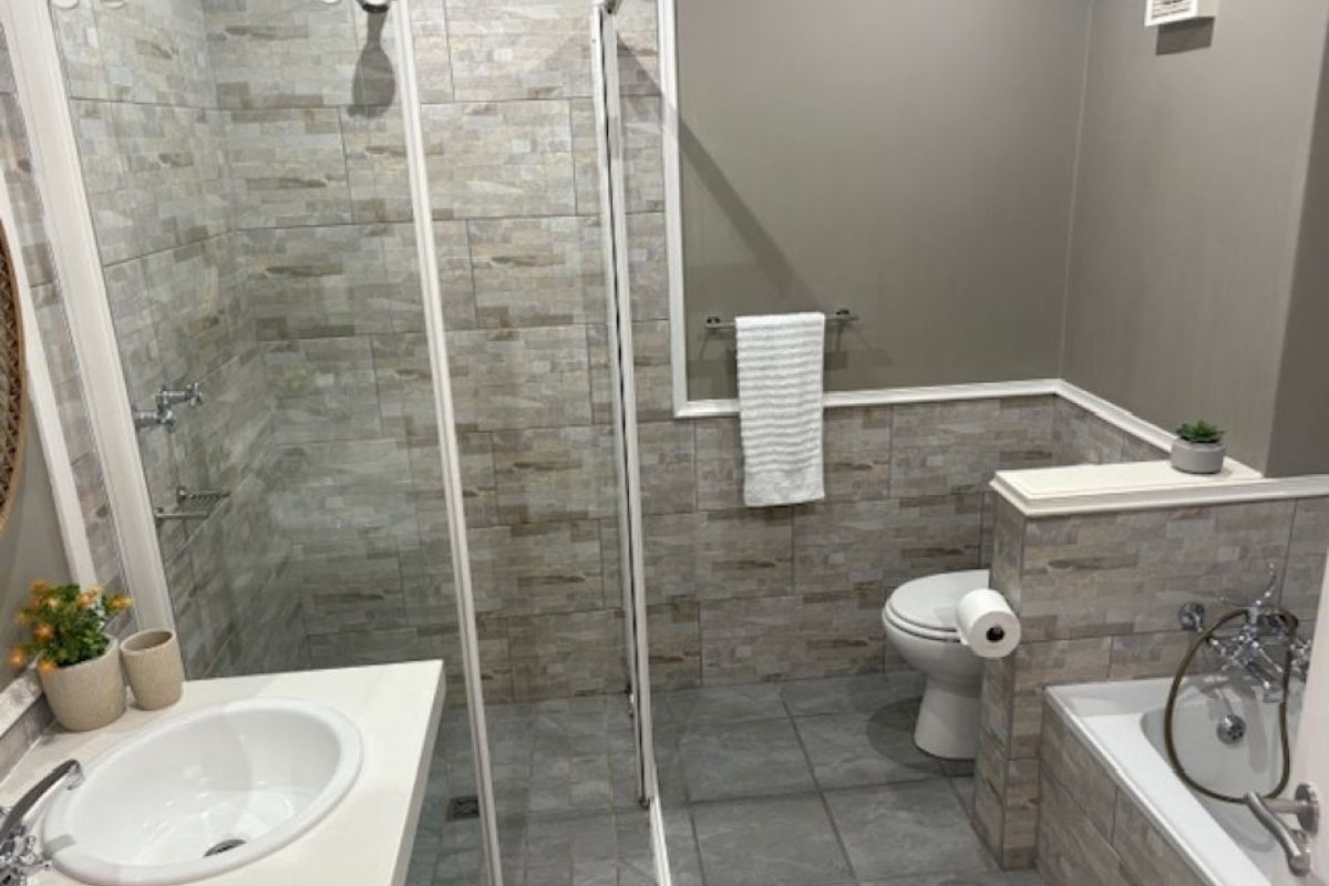 Modern bathroom featuring a walk-in shower with glass enclosure, a built-in bathtub, wall-mounted toilet, and contemporary tiled finishes throughout.